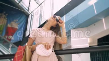 年轻有魅力的女孩站在商场里，摘下太阳镜，拎包，购物理念，时尚理念